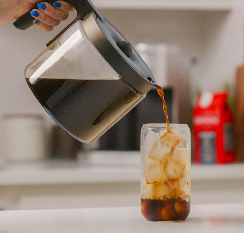 Hand pouring cool coffee over glass of ice to make iced coffee